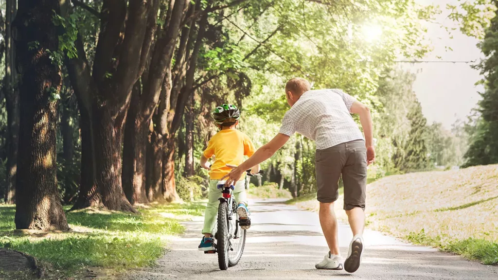 Representing Children in Family Court Proceedings - Representing Children Solicitors - Picture of a child on a bike being helped along by their father.