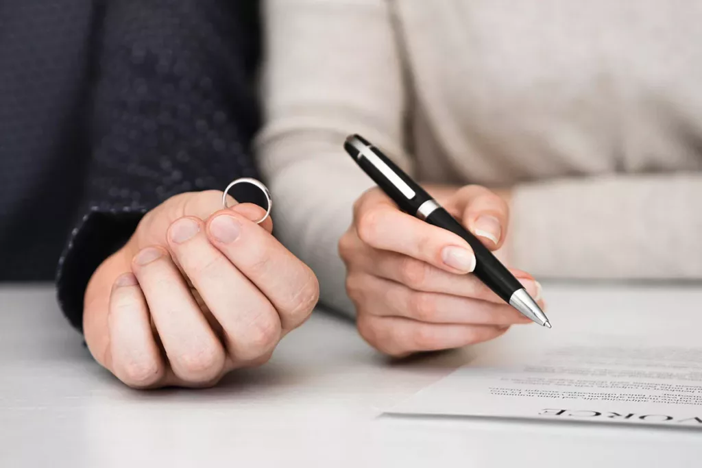 Separation Divorce Finances - Picture of a hand holding a wedding ring and another holding a pen about to sign divorce papers